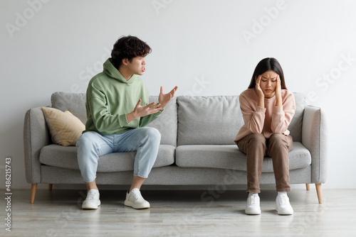 Misunderstanding in relationships. Millennial Asian couple quarrelling on couch at home, man shouting at his wife