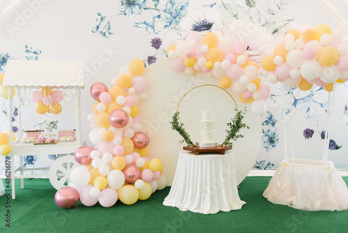 Obraz na płótnie A large three-tiered white cake for the baptism of a child with green twigs on the background of a beautiful photo zone with balloons and a candy bar w salonie