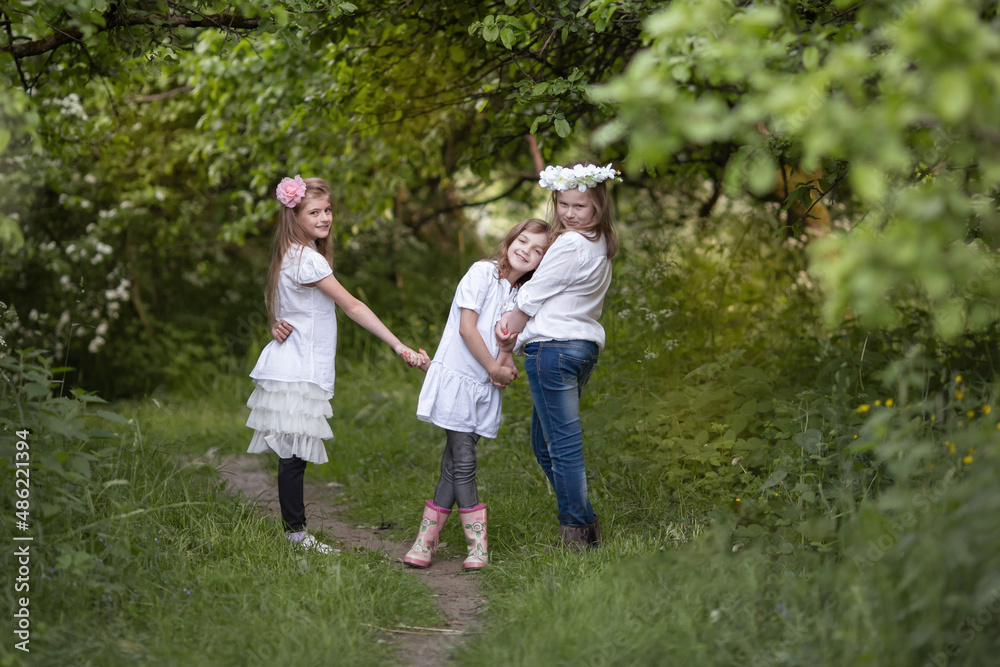 Three teenage girls in white blouses are laughing and playing, friendly hugging.  Children's fun in nature in summer, holidays, happy childhood concept