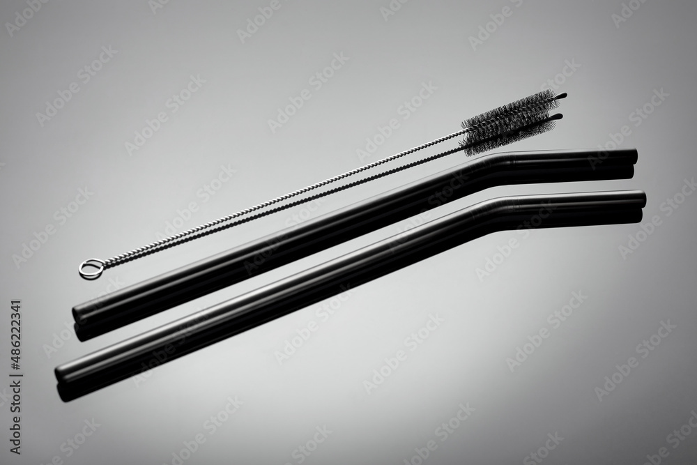 A small brush and reusable straws for drinks on a gray glossy background. Ecology protection concept A small brush and reusable straws for drinks on a gray glossy background. Ecology protection concept