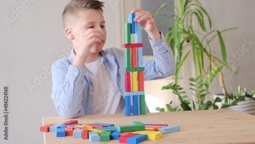 boy is playing with colored wooden bricks by building tower. Motor skills improvement. Play game at home photo
