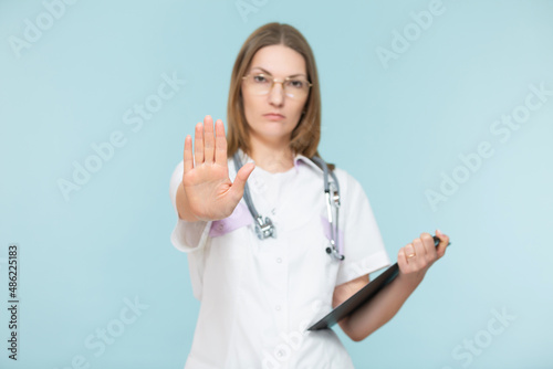 Beautiful woman doctor with a stethoscope and a black tablet  shows a stop sign with her hand  on a blue background. Copy paste. healthcare concept. Let s stop the disease.