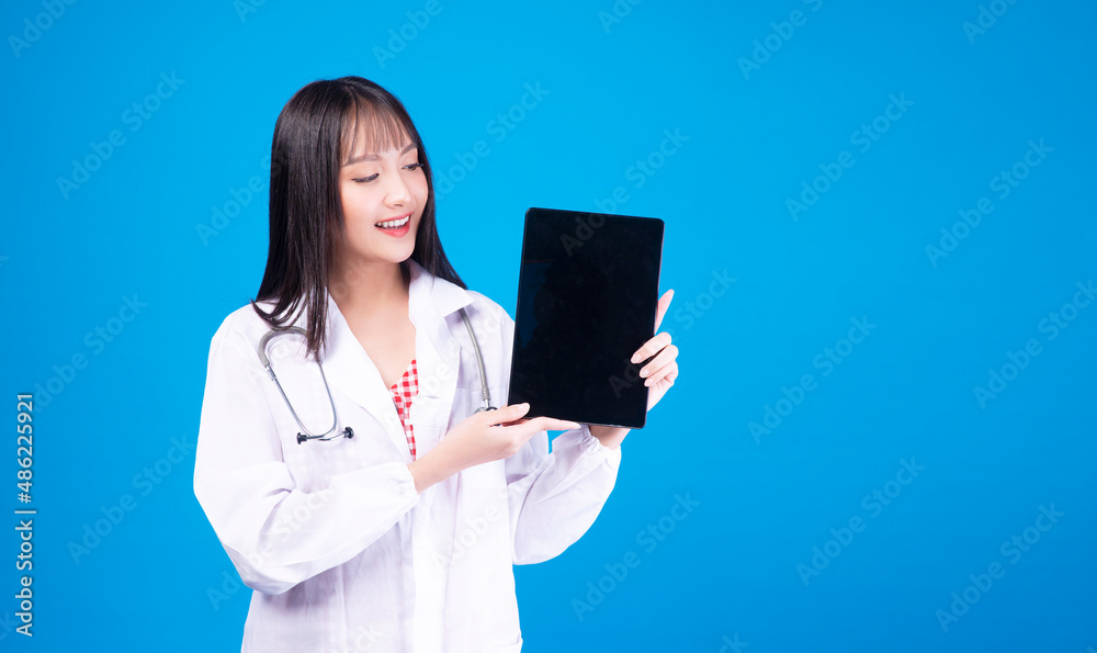 Professional pharmacist, doctor, nurse Asian woman wear laboratory coat with stethoscope showing tablet in hands present job standing over isolated blue background. Health care technology concept. Professional pharmacist, doctor, nurse Asian woman wear laboratory coat with stethoscope showing tablet in hands present job standing over isolated blue background. Health care technology concept.