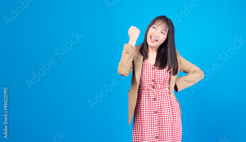 Excited business asian woman holding fist arms hand smile happiness success job or lucky standing over isolated blue background. Positive girl raised arms hand for new job. Lifestyle  winner concept.