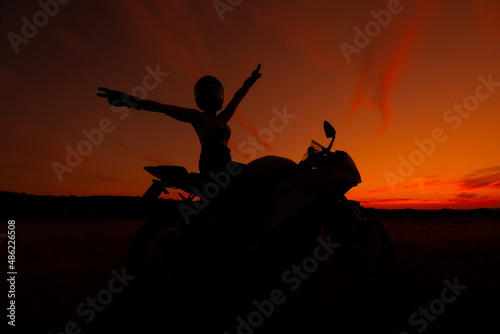silhouette of a biker woman wearing safety helmet with open arms on her motorcycle at sunset