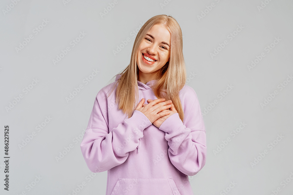 Happy young woman makes gratitude gesture presses palms to heart feels touched pleased by compliments says thank you expresses thankfullness, gray background. Body language and real feelings concept Happy young woman makes gratitude gesture presses palms to heart feels touched pleased by compliments says thank you expresses thankfullness, gray background. Body language and real feelings concept