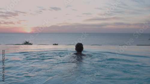 Young woman relaxing in swimming pool and enjoying beautiful sunset view of ocean. Vacation holidays photo