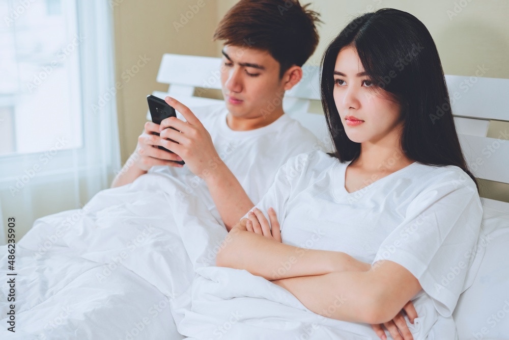 unhappy young asian couple have problems in relationships, boyfriend playing games on mobile phone on bed. unhappy young asian couple have problems in relationships, boyfriend playing games on mobile phone on bed.