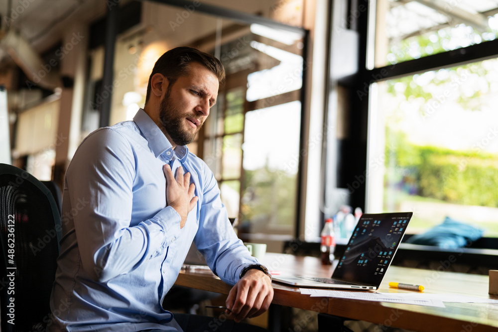 Young businessman having chest pain. Man sitting in the office working on laptop. Young businessman having chest pain. Man sitting in the office working on laptop.