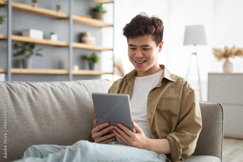 Smiling asian man using digital tablet at home Smiling asian man using digital tablet at home