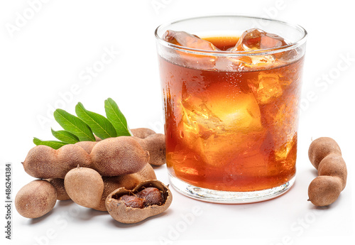 Glass of cool refreshing tamarind drink and some tamarind fruit on white background.