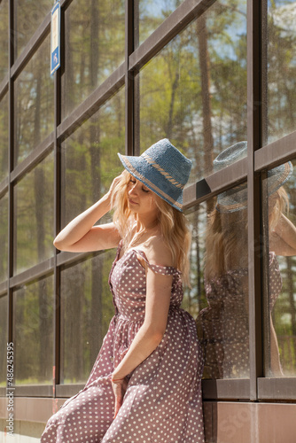 Beautiful blonde in a sundress and a hat on the background of a glass building

