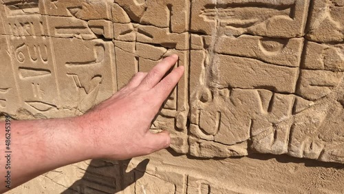 Man touches her hand to a wall with ancient Egyptian hieroglyphs and drawings of a statue photo