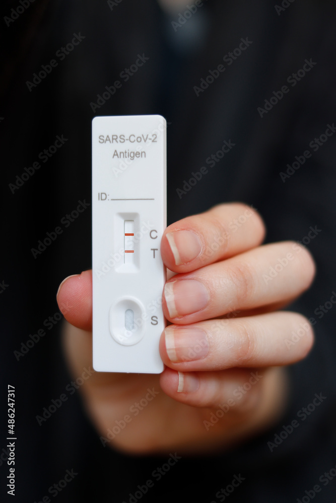 Rapid test for the detection of coronavirus, pandemic disease (COVID-19), with a positive, held by a hand. Two red lines in the antigen test, SARS-CoV-2. Black background Rapid test for the detection of coronavirus, pandemic disease (COVID-19), with a positive, held by a hand. Two red lines in the antigen test, SARS-CoV-2. Black background