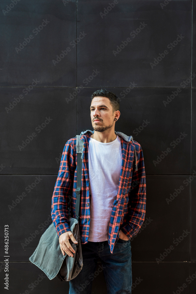 Stylish young international student standing outdoors with a bag on his shoulder on a sunny day.