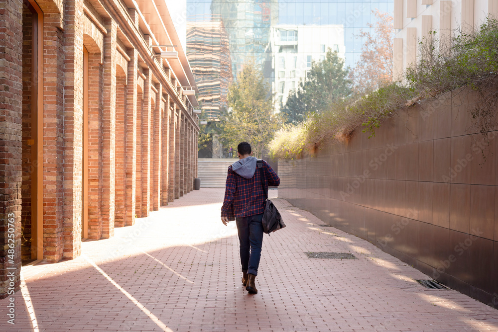 Rear view of a attractive young man holding shoulder bag walking through the city