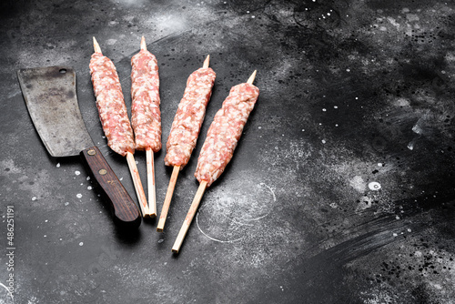 Fresh Raw kofta or lula kebabs skewers, on black dark stone table background, with copy space for text photo