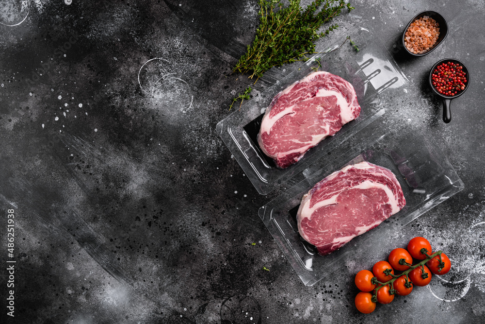 Raw steak of marbled beef in vacuum plastic pack, on black dark stone table background, top view flat lay, with copy space for text