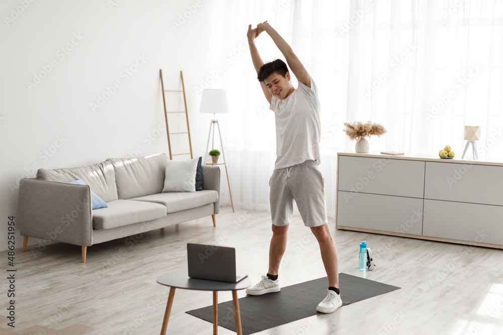 Asian guy doing stretching exercise watching online tutorial Asian guy doing stretching exercise watching online tutorial