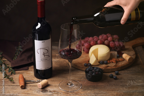 Woman pouring red wine into glass and appetizers on wooden table, closeup