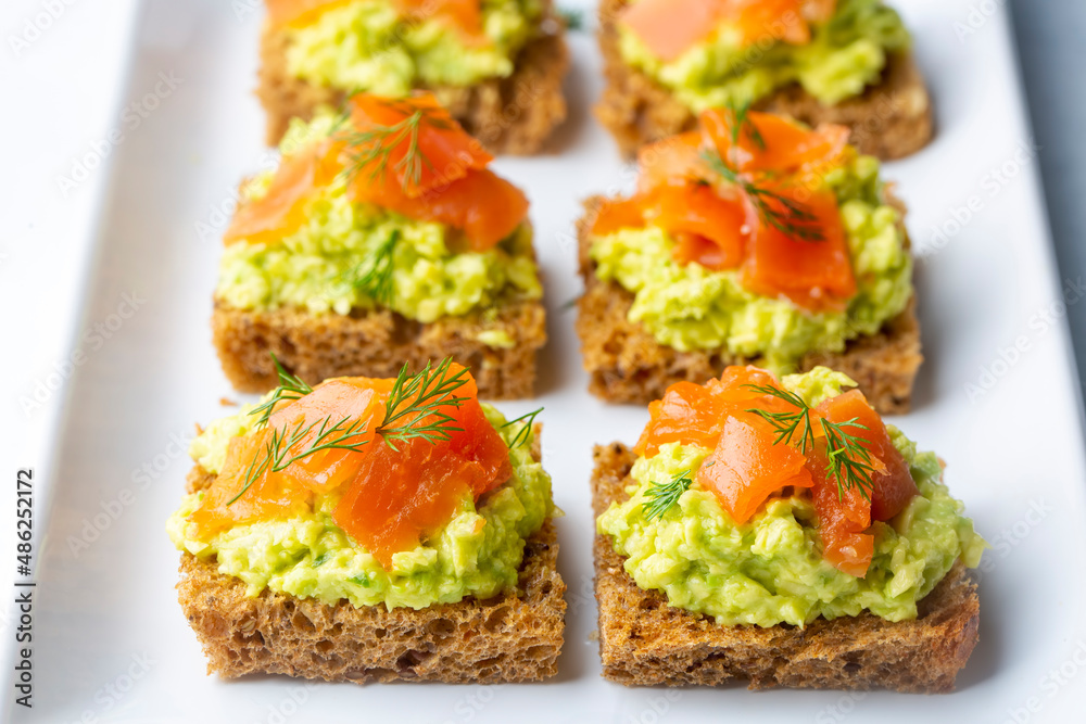 Toasts with avocado and smoked salmon on the wooden plate
