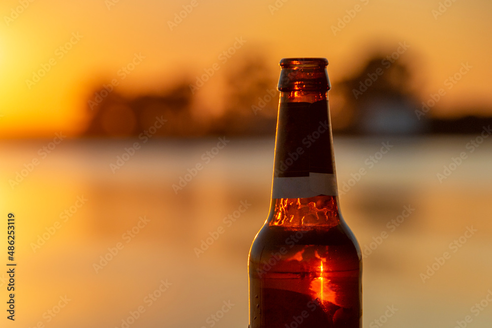 beer bottle in front of the river with sunset lighting the glass beer bottle in front of the river with sunset lighting the glass