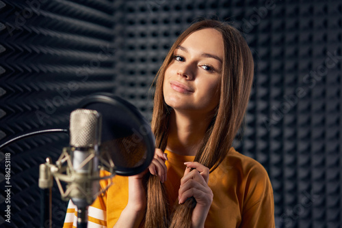 Teen girl in recording studio with mic over acoustic panel background