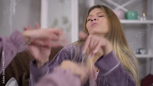 Portrait of rude young beautiful woman showing tongue fighting hands with friend indoors. Irritated annoyed Caucasian millennial lady arguing quarreling at pajama party gesturing photo