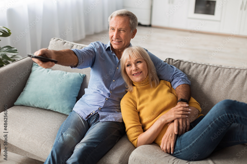 Happy Senior Spouses Watching TV Relaxing At Home