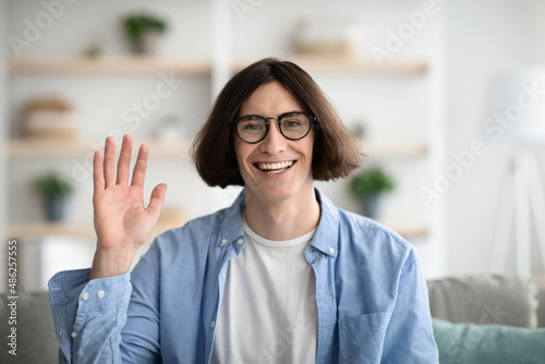 Greeting gesture concept. Happy young guy waving hand to camera and smiling, gesturing hi, making video call © Prostock-studio
