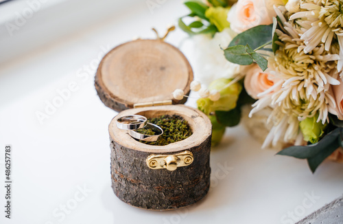 Wedding rings lie on greenery in a round wooden box, against the background of flowers. selective focus