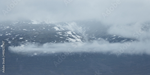 View of the mountains in the clouds. Snow on the slopes of the mountains. Poor visibility in cloudy weather. Natural background. © Andrei Stepanov