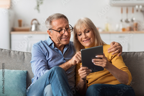 Mature Husband And Wife Using Tablet Embracing Sitting At Home