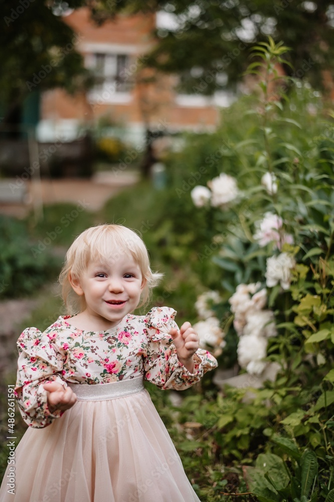 A two-year-old girl runs around the garden in a fluffy skirt in a park with peonies.