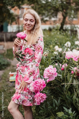 Beautiful smiling woman with a peony in her hands in a park with peonies