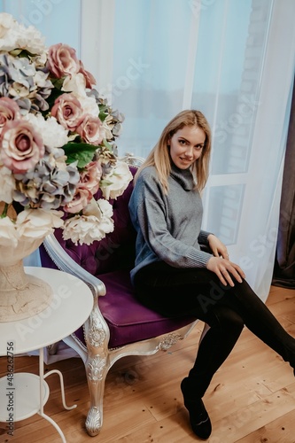 a girl in a shiny sweater is sitting on a chair next to a white stone vase with flowers