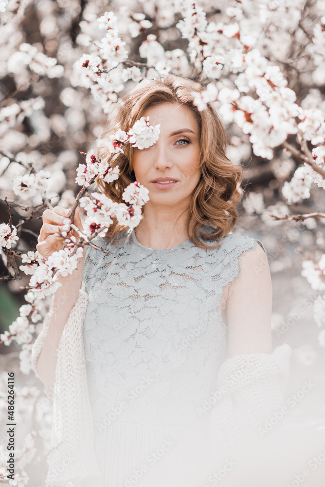 Portrait of pretty blong girl posing against the spring blooming trees in the garden.