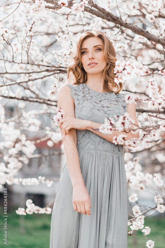 Portrait of pretty blong girl posing against the spring blooming trees in the garden.