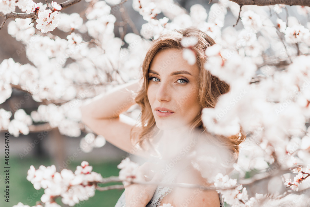 Portrait of pretty blong girl posing against the spring blooming trees in the garden.