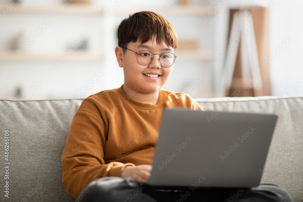 Cheerful chinese kid sitting on couch with laptop at home Cheerful chinese kid sitting on couch with laptop at home
