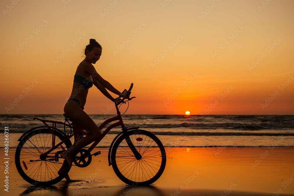 Fototapeta premium healthy alone woman ride on bicycle on empty sunset Goa India beach