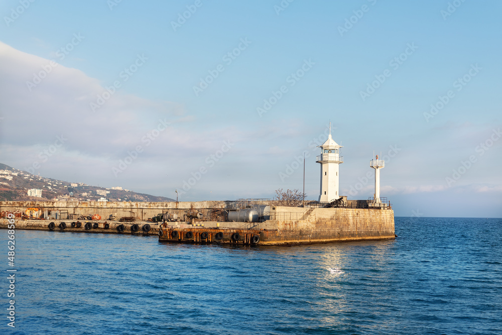 Scenic cityscape view old ancient white lighthouse building on stone pier at Yalta Crimean harbor on Black sea on warm sunny day. Bay nautical beacon house tower