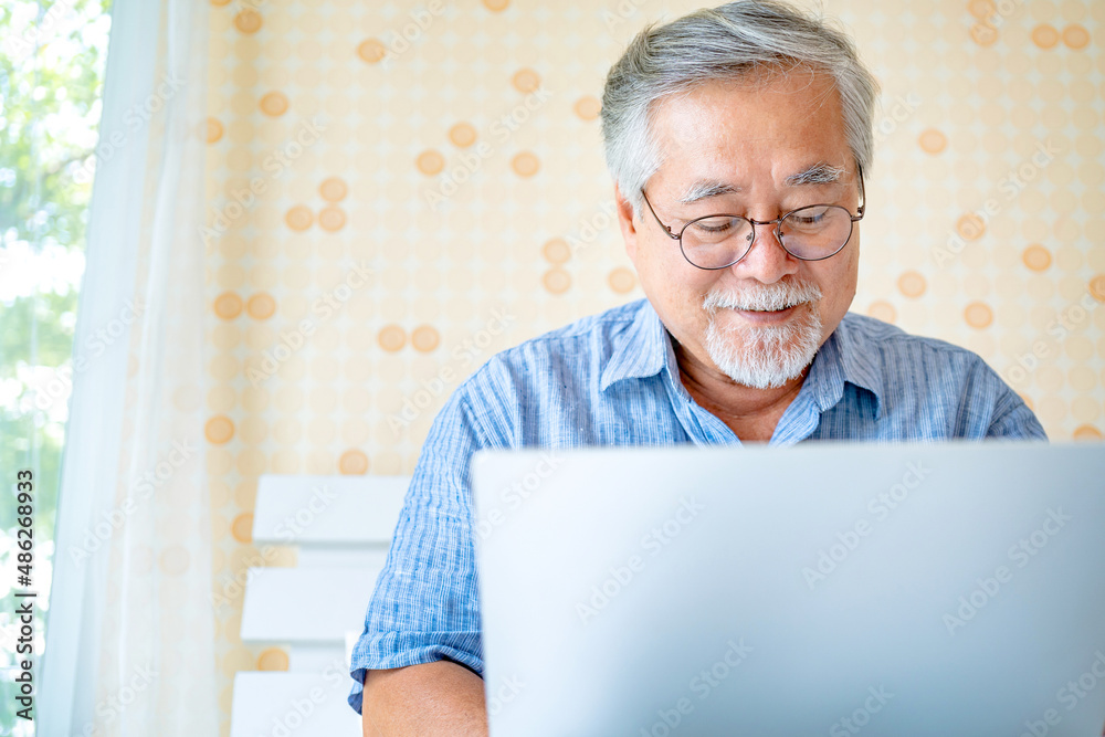 Happy old man positive, Portrait Asian Senior man and eyeglasses using computer laptop in bedroom at home, Old elderly male Technology communication retirement lifestyles concept. Happy old man positive, Portrait Asian Senior man and eyeglasses using computer laptop in bedroom at home, Old elderly male Technology communication retirement lifestyles concept.