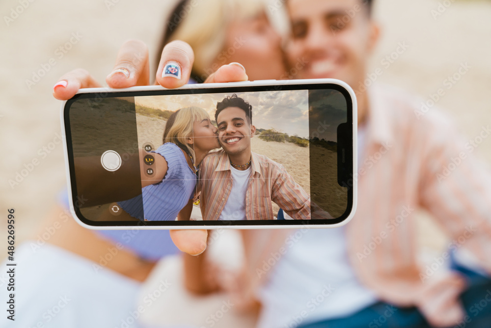 Young multiracial couple taking selfie photo on cellphone on beach
