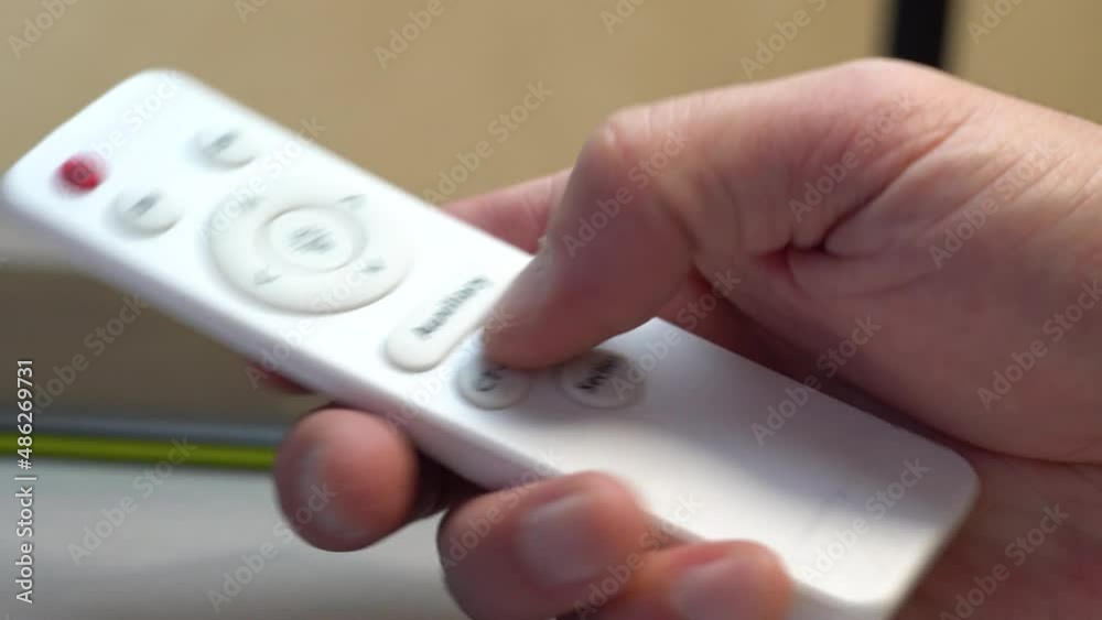 Remote control in a man's hand. White plastic. Light adjustment. Pressing buttons. Smart House. Wireless technologies. Change of lighting in the room. Brightness adjustment. Cold and warm light. Close Remote control in a man's hand. White plastic. Light adjustment. Pressing buttons. Smart House. Wireless technologies. Change of lighting in the room. Brightness adjustment. Cold and warm light. Close
