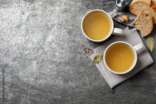 Hot delicious bouillon in cups on grey table, flat lay. Space for text