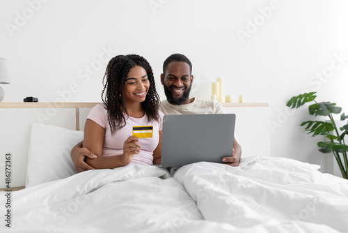 Smiling millennial african american guy with computer and lady with credit card shopping online