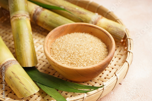 Brown sugar and sugar cane in a wooden tray on a beige background, close-up.