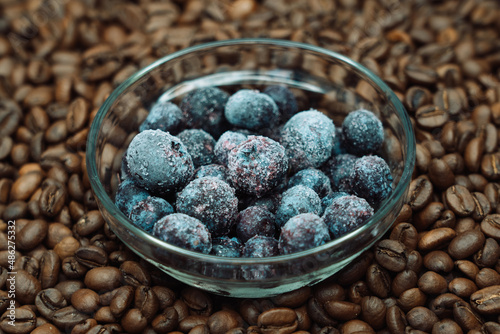 frozen blueberries in a glass transparent plate against the background of roasted coffee beans