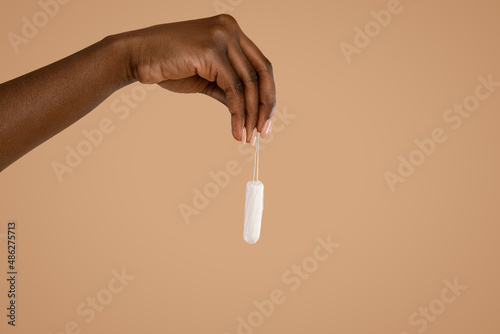 Hand of black woman holding tampon over beige studio background